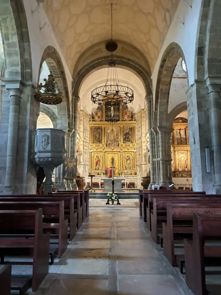 Interior de la iglesia del Monasterio de San Salvador de Cornellana, mostrando el retablo mayor barroco, las naves y el púlpito de piedra.