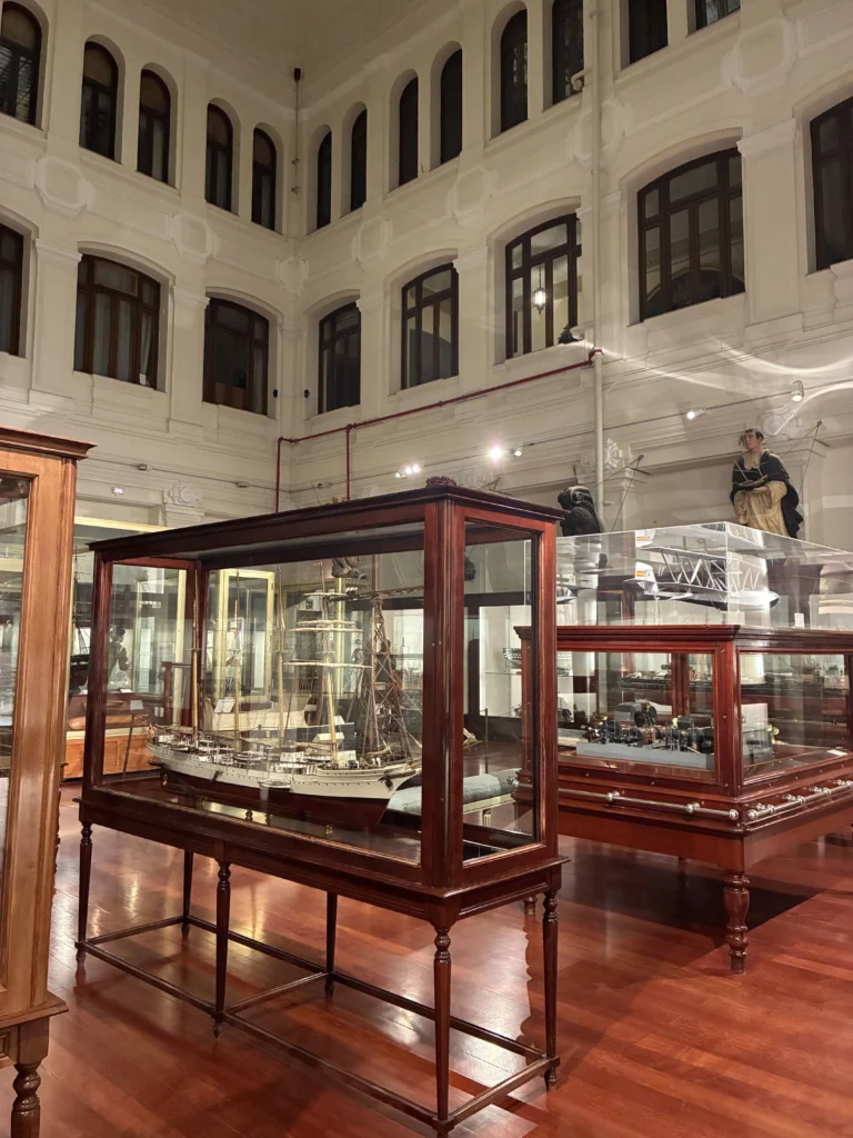 Sala principal del Museo Naval de Madrid con maquetas de barcos históricos en vitrinas de madera y vistas a la arquitectura interior del edificio.