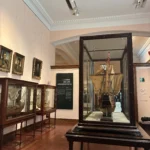 Sala "La Era de los Descubrimientos" en el Museo Naval de Madrid con modelos de barcos históricos en vitrinas de madera y retratos de navegantes.