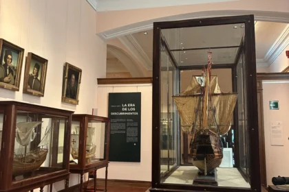 Sala "La Era de los Descubrimientos" en el Museo Naval de Madrid con modelos de barcos históricos en vitrinas de madera y retratos de navegantes.
