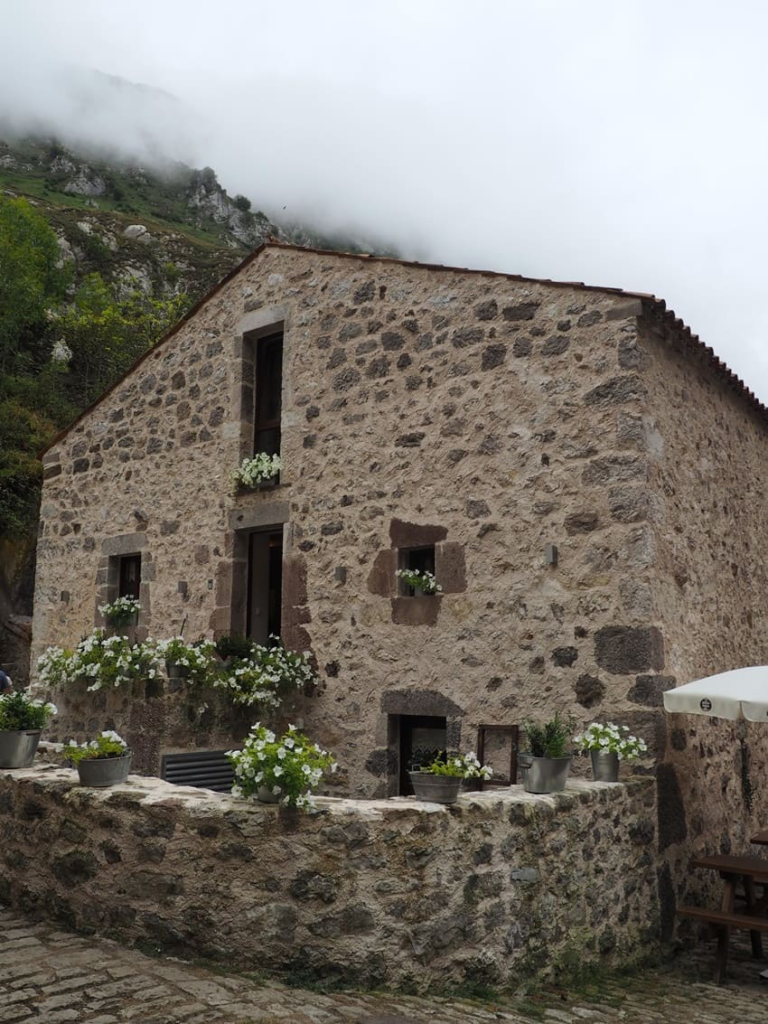 Fachada de casa rural tradicional en Bulnes construida en piedra con balcones decorados con flores blancas.