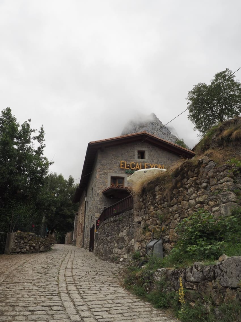 Restaurante y alojamiento El Caleyon en Bulnes, una casa de piedra tradicional bajo las cumbres nubladas de Picos de Europa.
