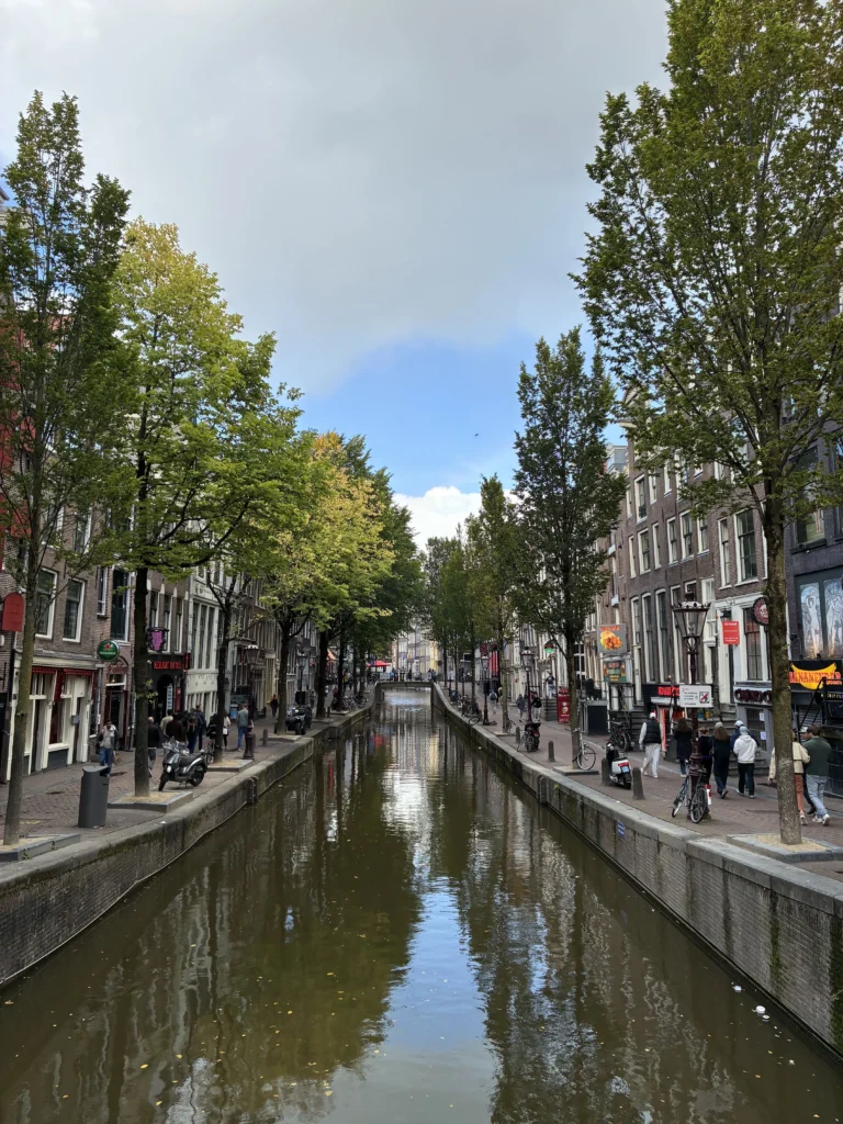Canal Oudezijds Achterburgwal en el Barrio Rojo de Ámsterdam con peatones paseando por los muelles arbolados.