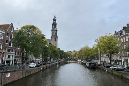 Canal Prinsengracht en Ámsterdam con el canal centrado y la torre de la iglesia Westerkerk destacando a la izquierda bajo un cielo nublado.