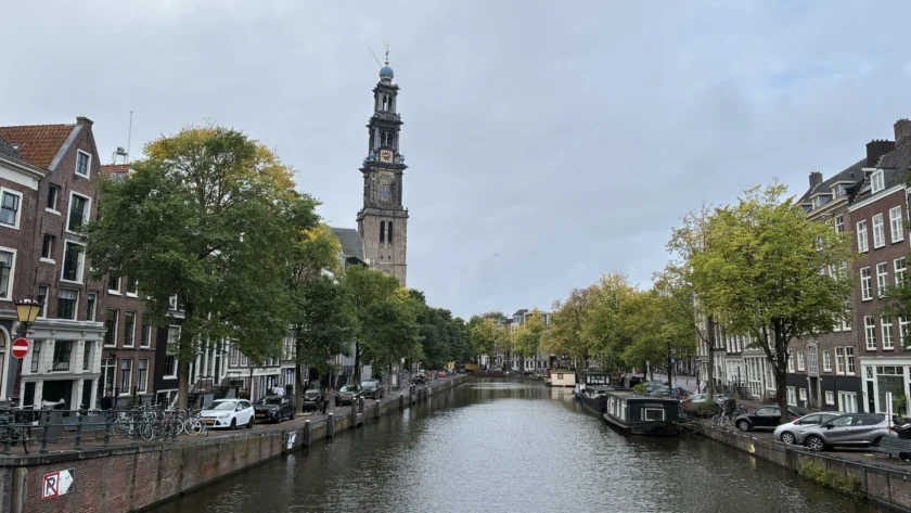 Canal Prinsengracht en Ámsterdam con el canal centrado y la torre de la iglesia Westerkerk destacando a la izquierda bajo un cielo nublado.