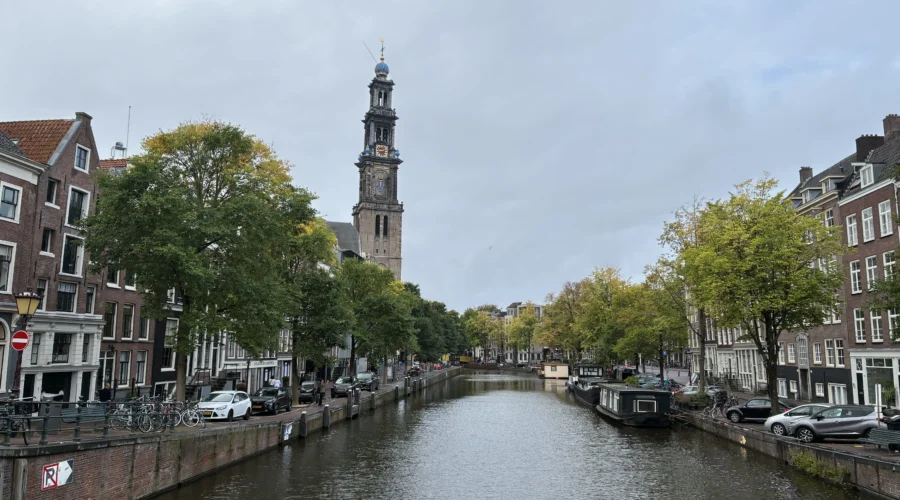 Canal Prinsengracht en Ámsterdam con el canal centrado y la torre de la iglesia Westerkerk destacando a la izquierda bajo un cielo nublado.